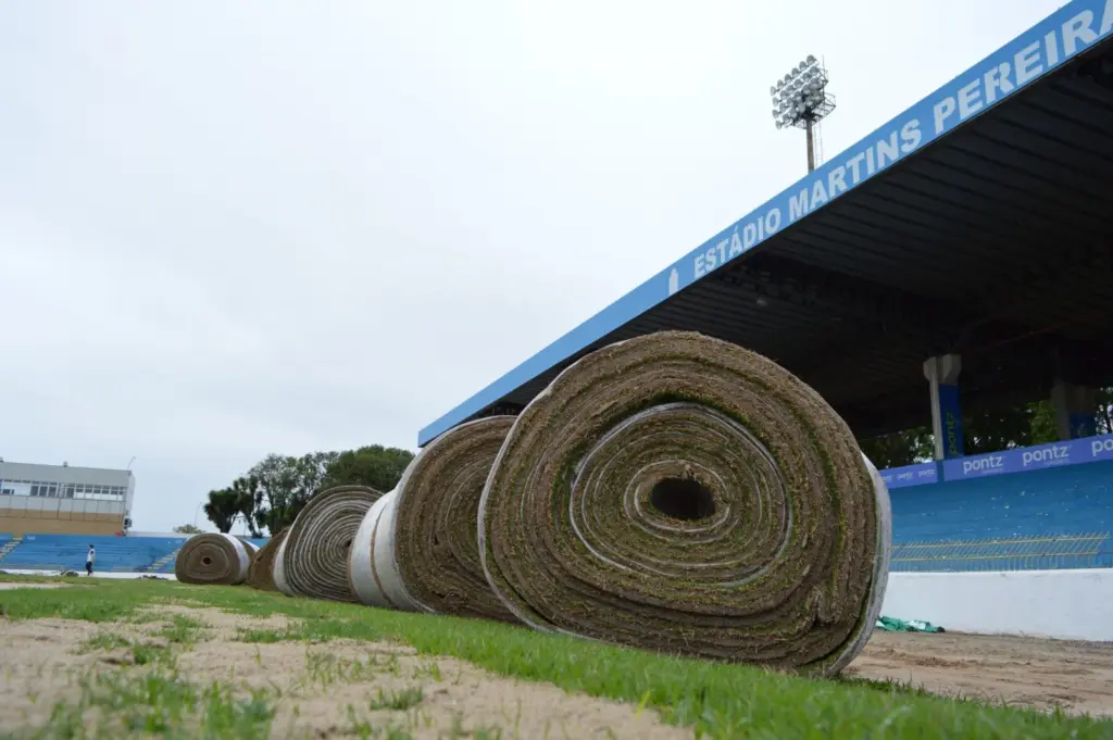 Equipe trabalha na instalação dos tapetes de grama na lateral do campo